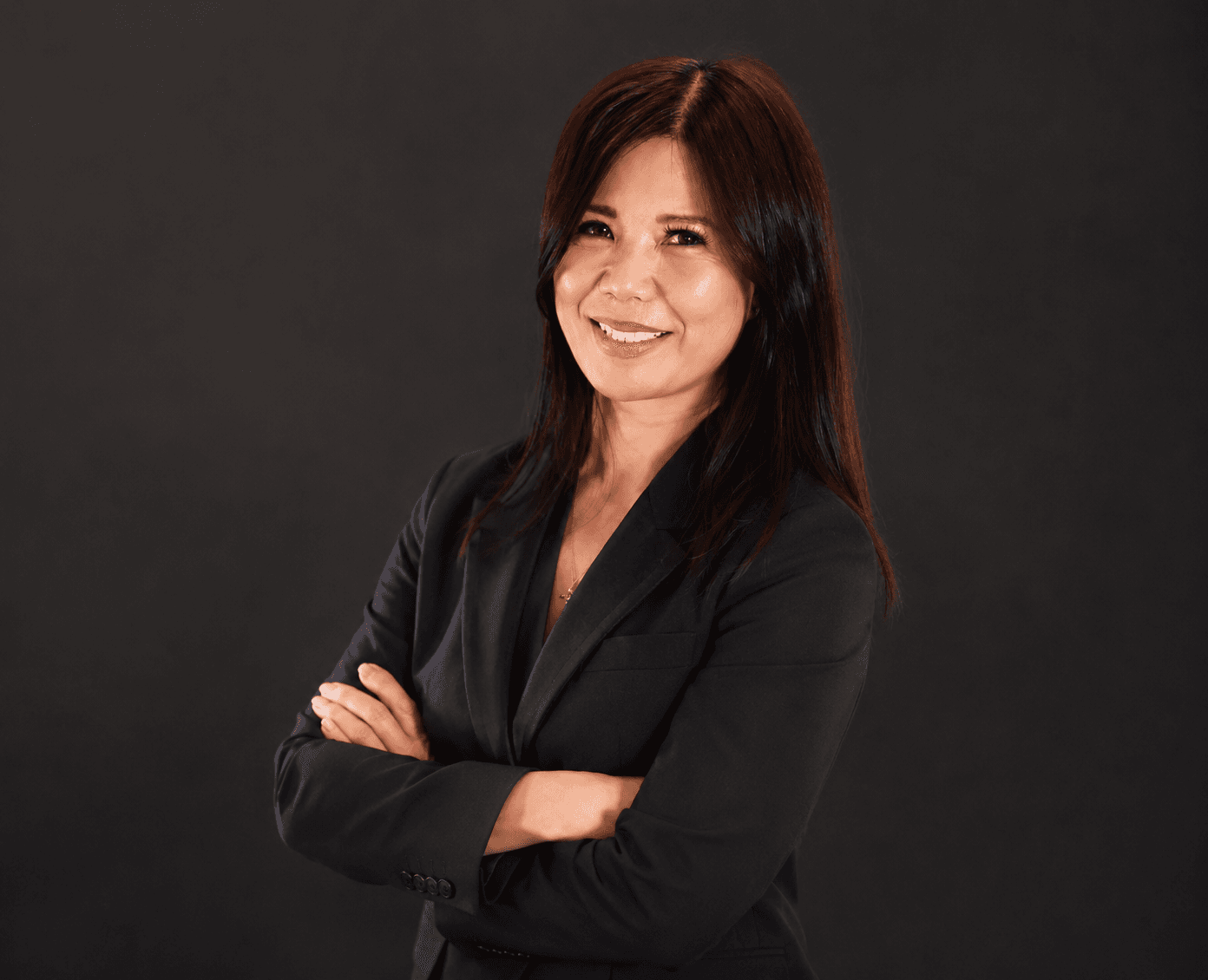 Smiling woman with dark hair in a black blazer, posing with her arms crossed.